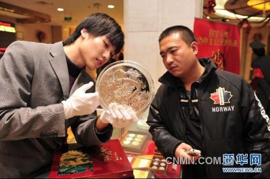 12月21日，工作人員向顧客介紹一款5公斤重的壬辰賀歲紀(jì)念大銀章，其正面的“金龍降喜”圖案，寓意對(duì)龍年萬(wàn)事亨通的美好祝福。